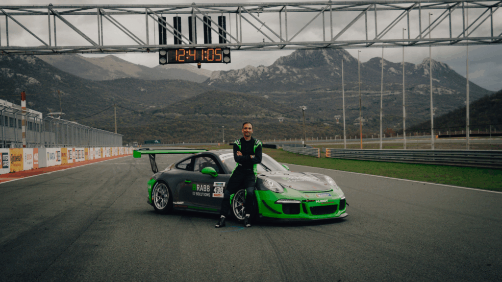 Rennfahrer im Rennanzug lehnt an einem Porsche 911 GT3 Cup von RABB Motors & Events auf einer Rennstrecke
